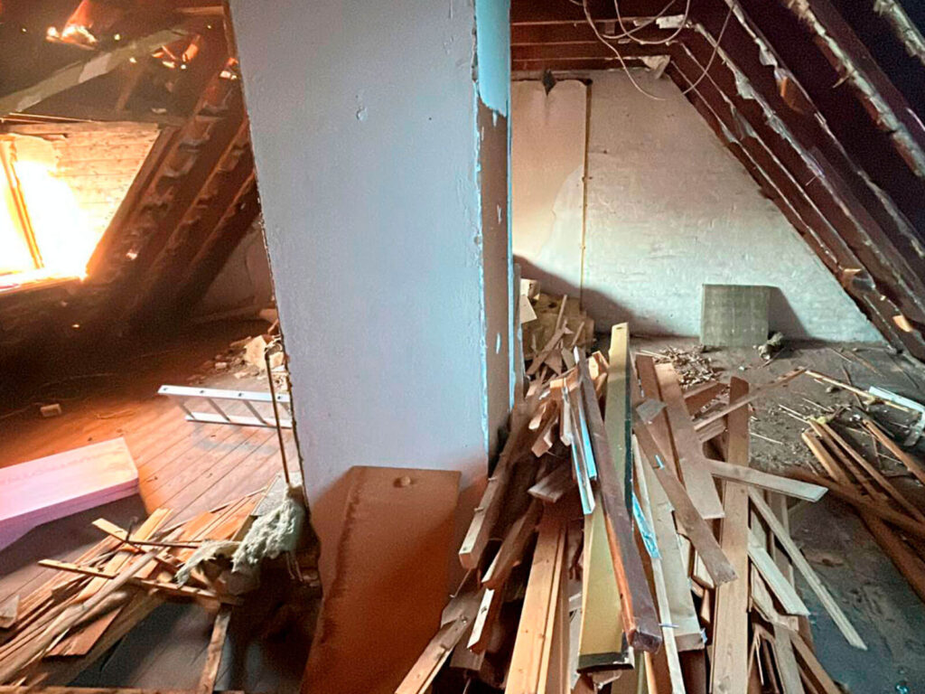 Vorherbild der Sanierung eines Obergeschosses, unterm Dach mit Schrägen. Schornstein in der Mitte des Raumes, Gaubenfenster sichtbar.